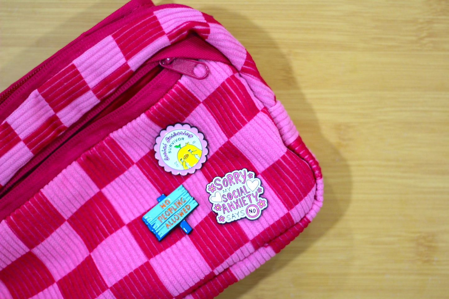 A pink and red checkered zippered pouch with three decorative stickers, placed on a light wood surface.