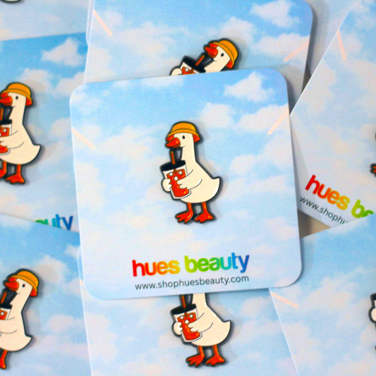 A close-up of several enamel pins attached to matching backing cards. The cards have a light blue sky and white cloud background, with a cartoon white goose wearing a yellow hard hat and holding a red coffee cup.