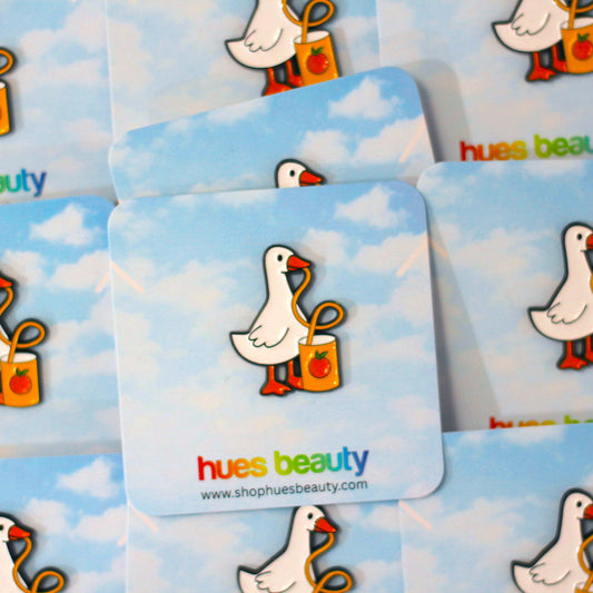 A close-up of multiple square cards or stickers featuring a cartoon white goose holding a yellow-orange gift bag against a light blue sky background. The word 'hues beauty' appears in multicolored lowercase text on several cards, with a website URL printed near the bottom.