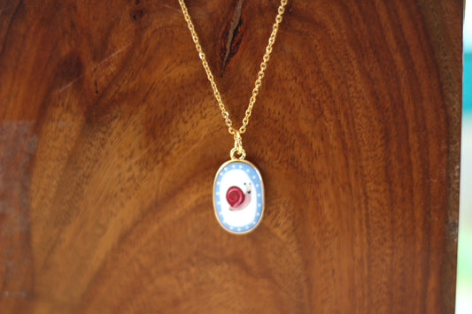 Gold chain necklace with an oval pendant featuring a blue and white design with a snail, displayed on a wooden surface.